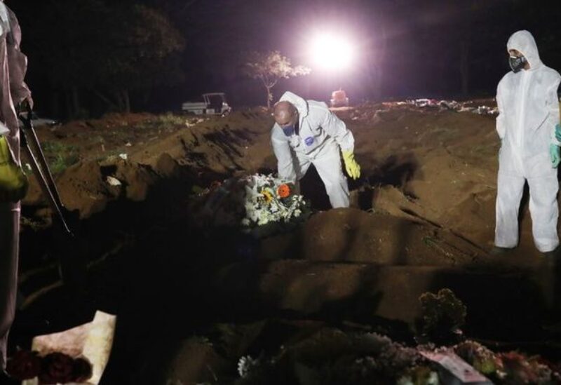 A gravedigger wearing a protective suit places flowers on a grave as spotlights illuminate during the first night burial at Vila Formosa cemetery, amid the coronavirus disease (COVID-19) pandemic, in Sao Paulo, Brazil, March 25, 2021.