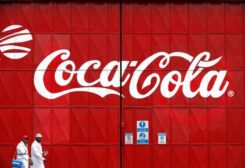 Workers walk past a Coca Cola logo painted on a gate at a Coca Cola factory in Nairobi, Kenya, June 7, 2018. REUTERS