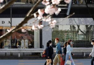 FILE PHOTO: Pedestrians wearing protective face masks amid the coronavirus disease (COVID-19) outbreak, are seen behind cherry blossoms in Tokyo, Japan, March 18, 2021.