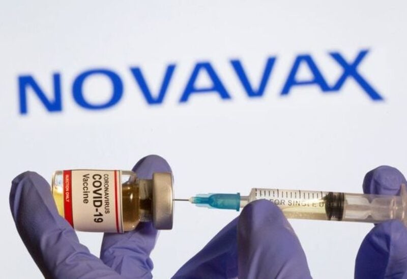 A woman holds a small bottle labeled with a "Coronavirus COVID-19 Vaccine" sticker and a medical syringe in front of displayed Novavax logo in this illustration taken, October 30, 2020.