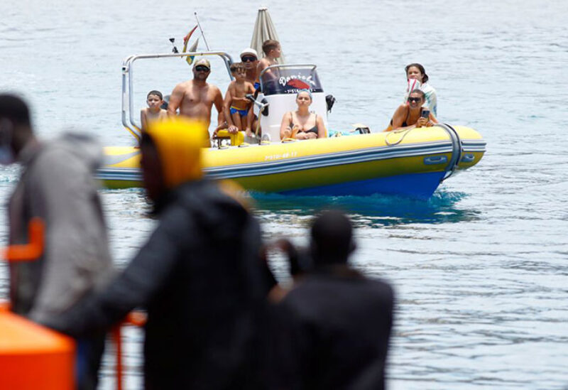 A group of tourists on a boat observes several migrants waiting to disembark from a Spanish coast guard vessel,