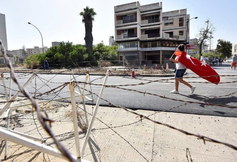 A woman walks while holding Turkish and Turkish Cypriot flags inside an area fenced off by the Turkish military since 1974, in the abandoned coastal area of Varosha, a suburb of the town of Famagusta in Turkish-controlled northern Cyprus, October 8, 2020. (Reuters/Harun Ucar)