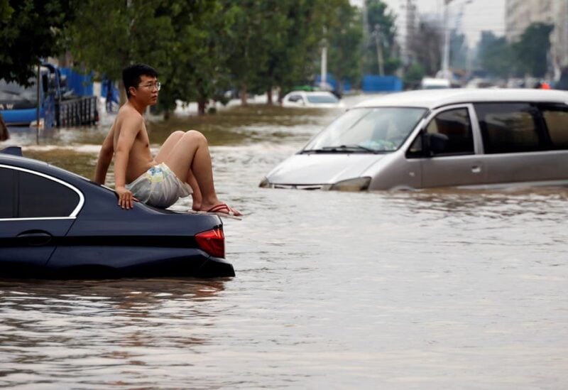 A man sits on a stranded vehicle on a flooded road following heavy rainfall in Zhengzhou, Henan province, China July 22, 2021. (Reuters)