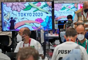 Journalists work as the making of a Tokyo 2020 mural is shown on television screens at the main press center of the 2020 Summer Olympics, on July 23, 2021, in Tokyo, Japan. (AP)