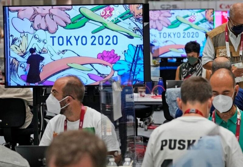 Journalists work as the making of a Tokyo 2020 mural is shown on television screens at the main press center of the 2020 Summer Olympics, on July 23, 2021, in Tokyo, Japan. (AP)
