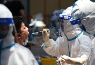 A medical worker in protective suit collects a swab from a resident for nucleic acid testing at a sports centre in Jiangning district, following new cases of the coronavirus disease (COVID-19) in Nanjing, Jiangsu province, China July 21, 2021. (Reuters)