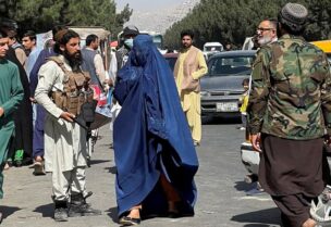 Taliban forces block the roads around the airport, while a woman with Burqa walks passes by, in Kabul, Afghanistan. August 27, 2021. (Reuters)