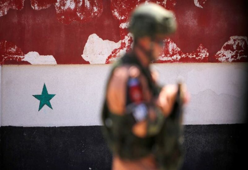 A file photo shows a Russian soldier stands guard near a Syrian national flag drawn on awall in Homs, Syria.