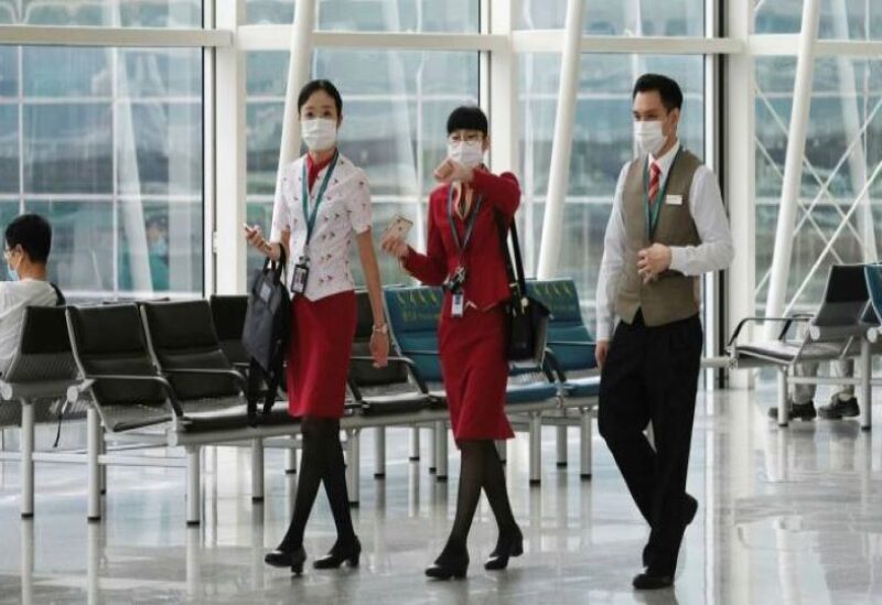 A flight attendant walks under an information board at the arrivals hall of Hong Kong International Airport,