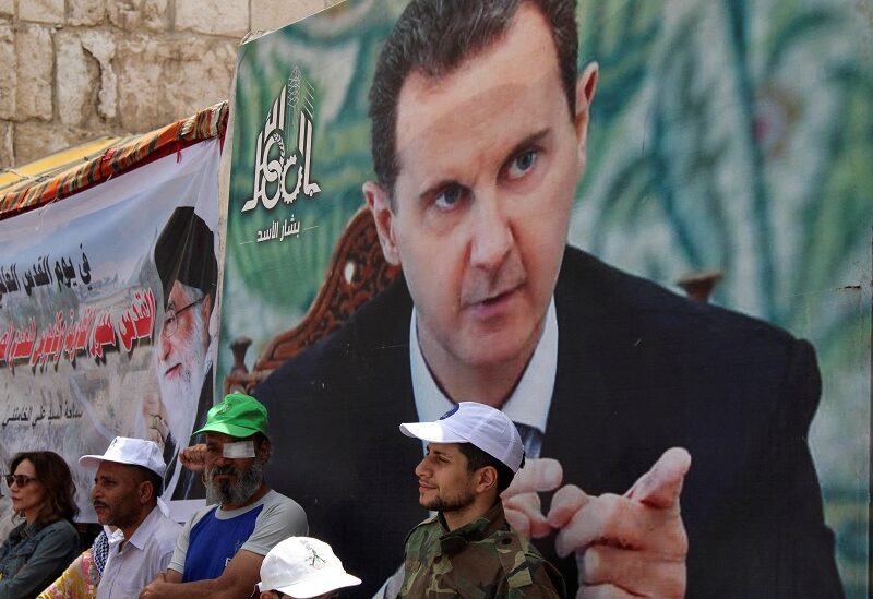 FILE PHOTO: Syrians and Palestinians living in Syria stand next to a poster depicting Syria's President Bashar al-Assad as they mark the annual al-Quds Day (Jerusalem Day), in Damascus, Syria April 29, 2022. REUTERS/Firas Makdesi/File Photo