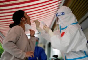 A medical worker in a protective suit collects a swab sample from a resident for nucleic acid testing, outside a closed entrance of a building during lockdown, amid the coronavirus disease (COVID-19) pandemic, in Shanghai, China, May 12, 2022. REUTERS/Aly Song