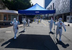 Workers in protective suits move equipment for a makeshift nucleic acid testing site to the next residential area after wrapping up the screening at a compound, amid the coronavirus disease (COVID-19) outbreak in Shanghai, China May 14, 2022. Picture taken May 14, 2022. cnsphoto via REUTERS