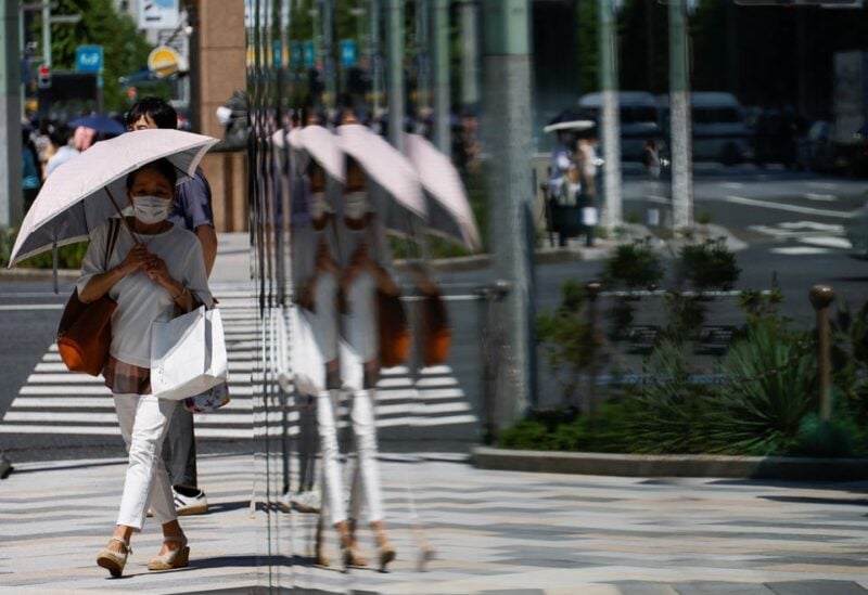 A woman holding an umbrella is reflected on a window while walking along a street, as the Japanese government issues a warning over a possible power crunch due to a heatwave in Tokyo, Japan June 28, 2022. REUTERS/Issei Kato