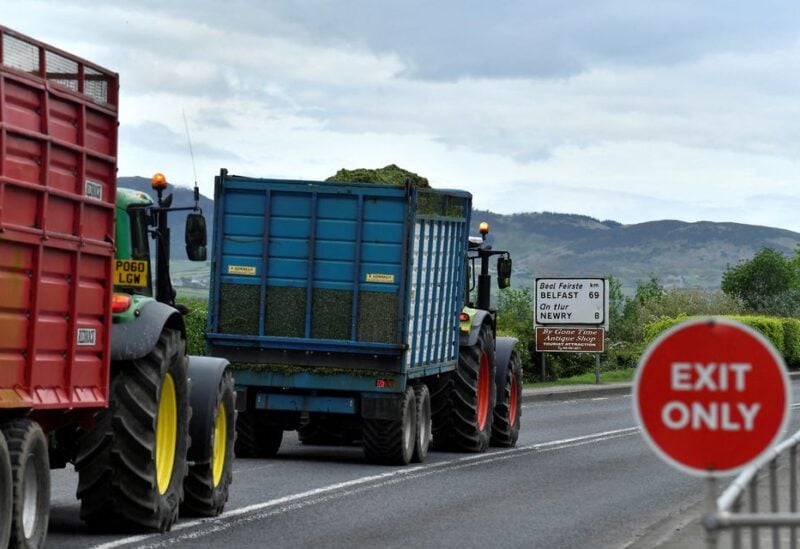 Tractors drive past an exit sign and a road sign for Belfast on the border between Northern Ireland and Ireland