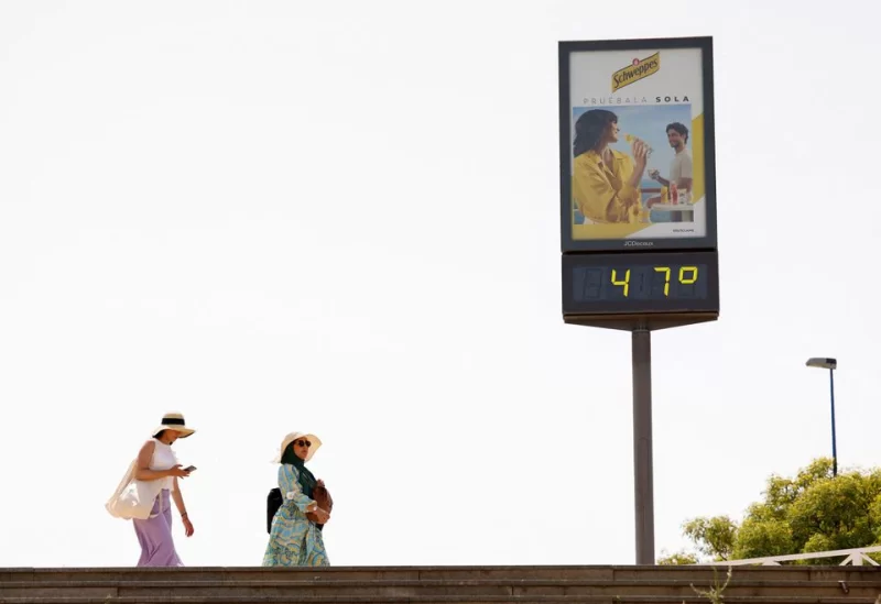 Women walk next to a thermometer displaying 47 Celsius degrees