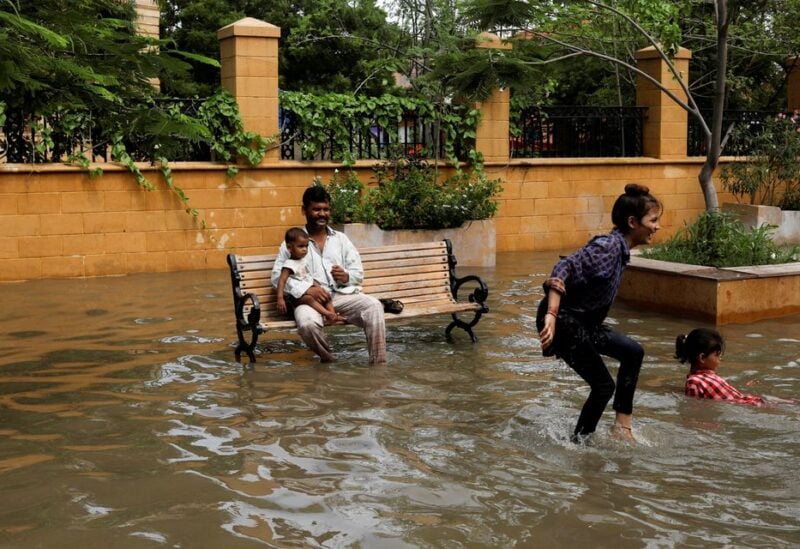 A man with a baby sits on a bench while children play amid flooded street during the monsoon season in Karachi, Pakistan July 11, 2022. REUTERS/Akhtar Soomro