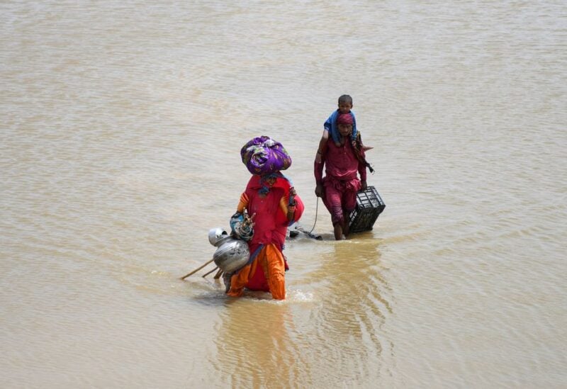 A family with their belongings wade through rain waters following rains and floods during the monsoon season in Jamshoro, Pakistan August 26, 2022. REUTERS/Yasir Rajput NO RESALES. NO ARCHIVES.