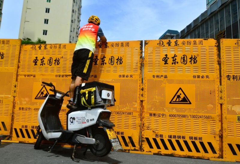 A courier stands on an electric bike to make a delivery over a barricade, amid lockdown measures to curb the coronavirus disease (COVID-19) outbreak in Sanya, Hainan province, China August 6, 2022. China Daily via REUTERS