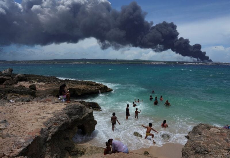 People enjoy the beach near the smoke of a fire over fuel storage tanks that exploded near Cuba's supertanker port in Matanzas, Cuba, August 6, 2022. REUTERS/Alexandre Meneghini