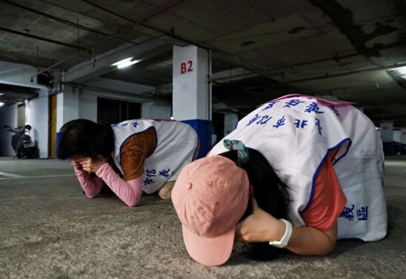 People demonstrate taking shelter with their hands covering their eyes and ears while keeping their mouth open, during a drill at a basement parking lot that will be used as an air-raid shelter in the event of an attack, in Taipei, Taiwan, July 22, 2022.