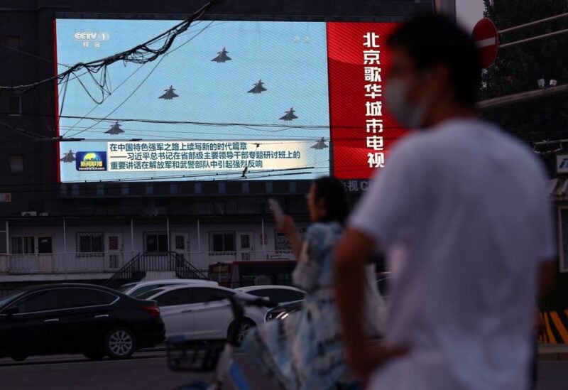 Pedestrians wait at an intersection near a screen showing footage of Chinese People's Liberation Army (PLA) aircraft during an evening news programme, in Beijing, China August 2, 2022
