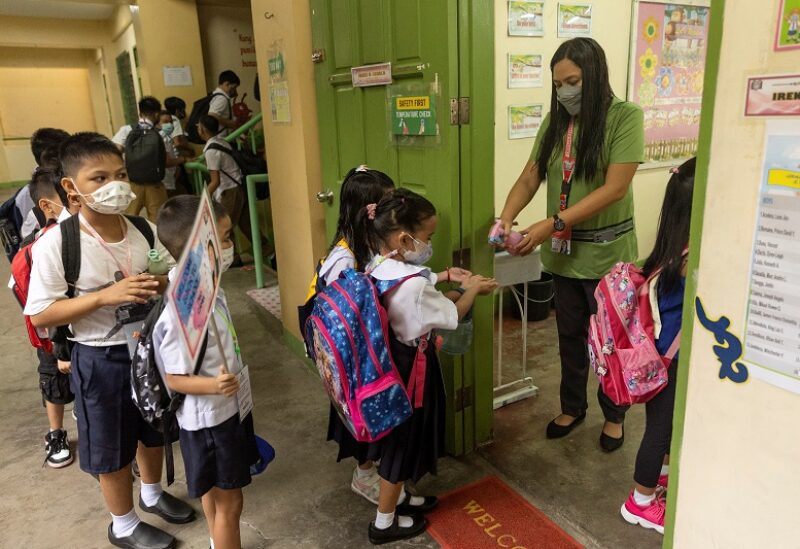 A teacher sprays alcohol on the hands of students for protection against the coronavirus disease (COVID-19), on the first day of in-person classes at a public school in San Juan City, Philippines, August 22, 2022. REUTERS/Eloisa Lope
