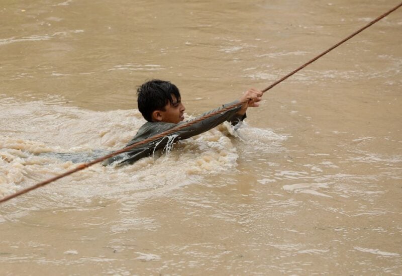 A boy crosses a flooded street, with the help of a wire fastened on both ends, following rains and floods during the monsoon season in Charsadda, Pakistan August 27, 2022