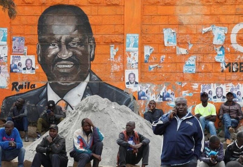 People sit next to a wall mural of Raila Odinga the presidential candidate for Azimio la Umoja and One Kenya Alliance