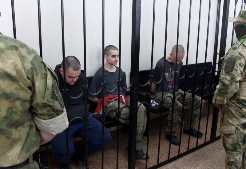 Two British citizens Aiden Aslin, left, and Shaun Pinner, right, and Moroccan Saaudun Brahim, center, sit behind bars in a courtroom in Donetsk, in the territory which is under the Government of the Donetsk People's Republic control, eastern Ukraine, Thursday, June 9, 2022. (AP Photo)