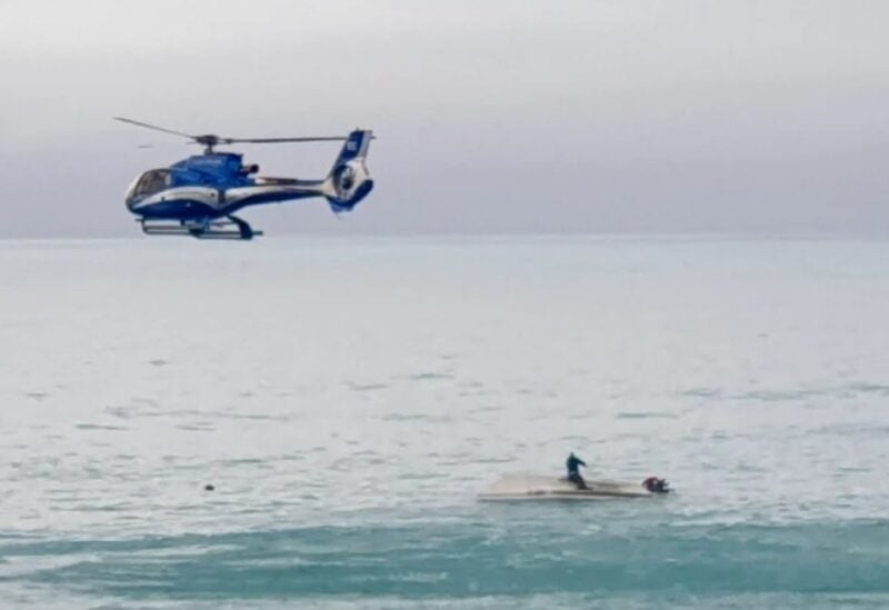 A helicopter flies over an upturned boat with a survivor sitting on the hull off the coast of Kaikoura, New Zealand, on Saturday, September 10, 2022 [AP]