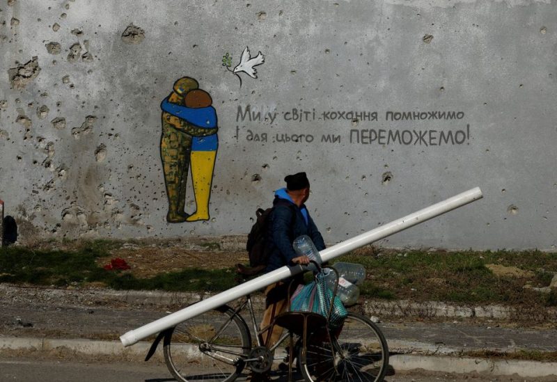 A man cycles past graffiti on a wall of a building covered with traces of bullets and shrapnel, amid Russia's attack on Ukraine, in the recently retaken town of Kupiansk, Ukraine, October 18, 2022. REUTERS/Clodagh Kilcoyne NO RESALES. NO ARCHIVES