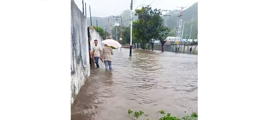 People walk through a flooded street in Maracay, Venezuela, October 6, 2022, in this screen grab obtained from a social media video. Carmen Elisa Pecorelli/via REUTERS