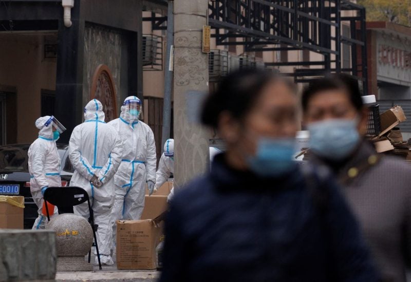 Residents walk near pandemic prevention workers in protective suits in a locked-down residential compound as outbreaks of the coronavirus disease (COVID-19) continue in Beijing, China November 18, 2022. REUTERS/Thomas Peter