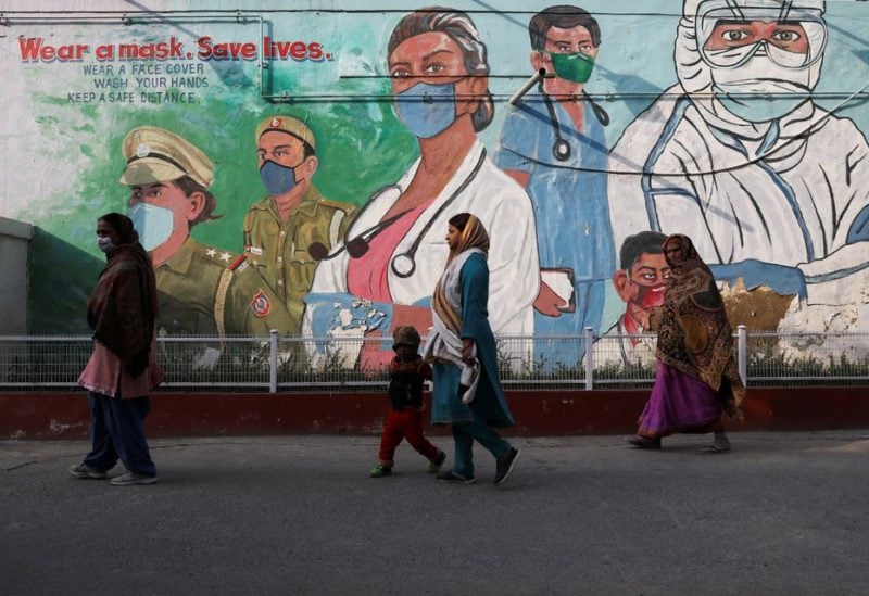 Women walk past a graffiti amidst the spread of the coronavirus disease (COVID-19) in New Delhi, India, February 7, 2022. REUTERS