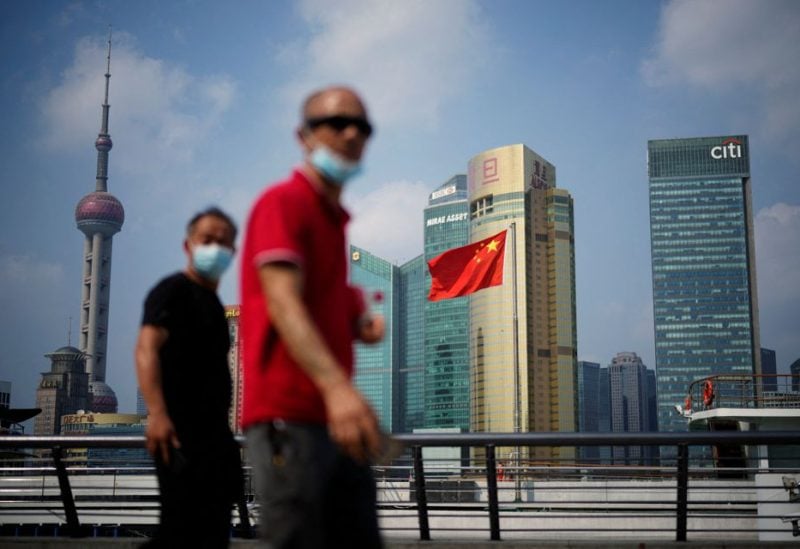People wearing face masks following the coronavirus disease (COVID-19) outbreak walk past a Chinese flag in Shanghai, China August 2, 2022. REUTERS