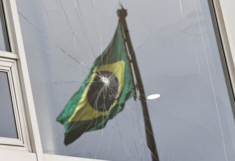 Brazil's flag is reflected on a broken window, after the supporters of Brazil's former President Jair Bolsonaro participated in an anti-democratic riot at Planalto Palace, in Brasilia, Brazil, January 9, 2023. REUTERS/Ueslei Marcelino