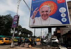 People walk next to the billboard of Pope Francis a day ahead of his arrival in Kinshasa, Democratic Republic of Congo January 30, 2023. REUTERS