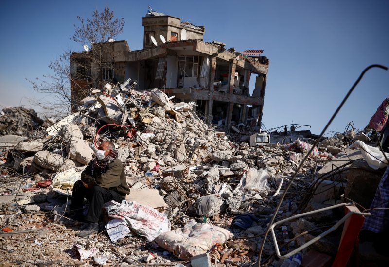 A man sits among rubble in the aftermath of a deadly earthquake in Kahramanmaras, Turkey February 11, 2023. REUTERS/Guglielmo Mangiapane