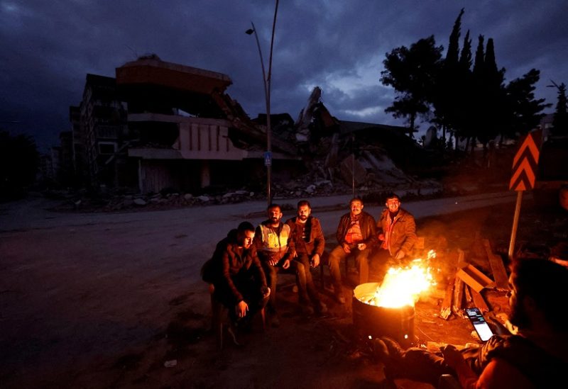 People warm themselves by a fire beside a collapsed building and rubble, in the aftermath of a deadly earthquake, in Antakya, Hatay province, Turkey, February 21, 2023. REUTERS/Clodagh Kilcoyne TPX IMAGES OF THE DAY