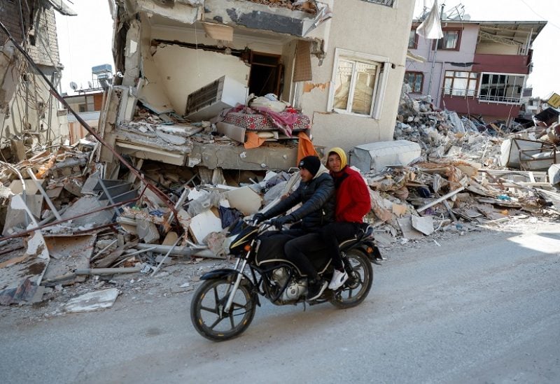 Men on a scooter ride past a destroyed home with a bed hanging out in the aftermath of a deadly earthquake in Hatay, Turkey February 14, 2023. REUTERS/Clodagh Kilcoyne