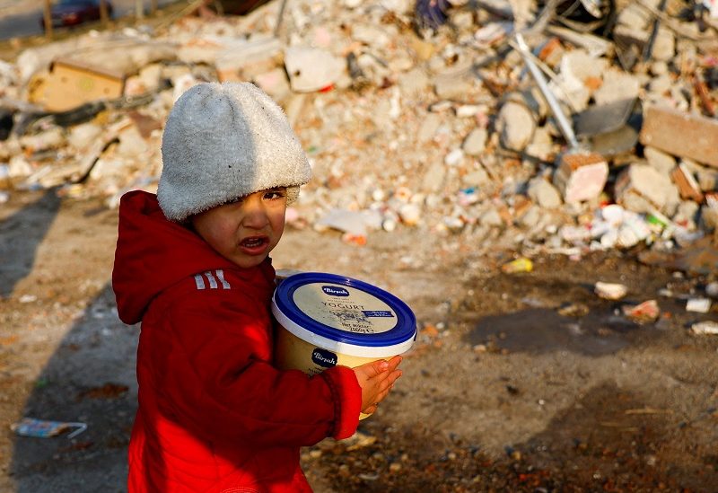A child holding a plastic container looks on amid rubble, in the aftermath of a deadly earthquake in Kahramanmaras, Turkey February 14, 2023. REUTERS/Suhaib Salem TPX IMAGES OF THE DAY