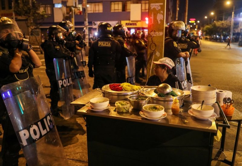 Riot police officers stand guard near a street food vendor during a protest to demand Peru's President Dina Boluarte to step down, in Lima, Peru, January 31, 2023. REUTERS/Sebastian Castaneda