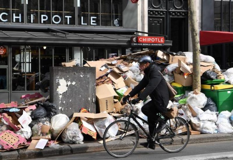 A cyclist drives past full waste bins in Paris' 2nd district as rubbish collectors strike against pension reforms, leaving many streets in the capital piled with stinking waste. (AFP)