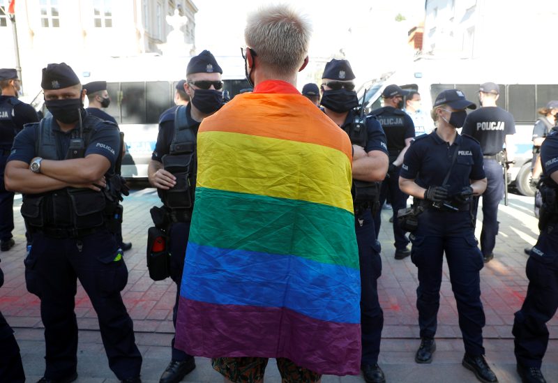 A pro-LGBT demonstrator wearing a rainbow flag stands in front of police officers as Polish nationalists gather to protest against what they call "LGBT aggression" on Polish society, in Warsaw, Poland August 16, 2020. REUTERS/Kacper Pempel