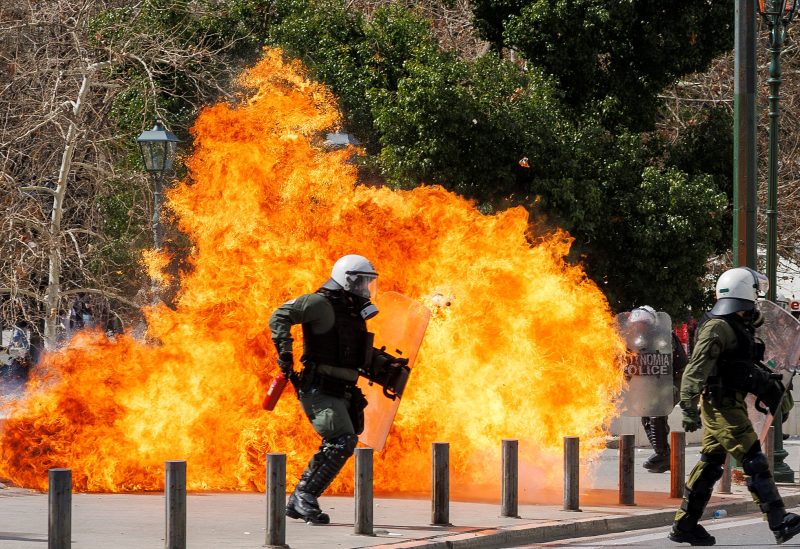 A riot police officer walks next to flames as clashes take place during a demonstration following the collision of two trains, near the city of Larissa, in Athens, Greece, March 5, 2023. REUTERS/Alkis Konstantinidis