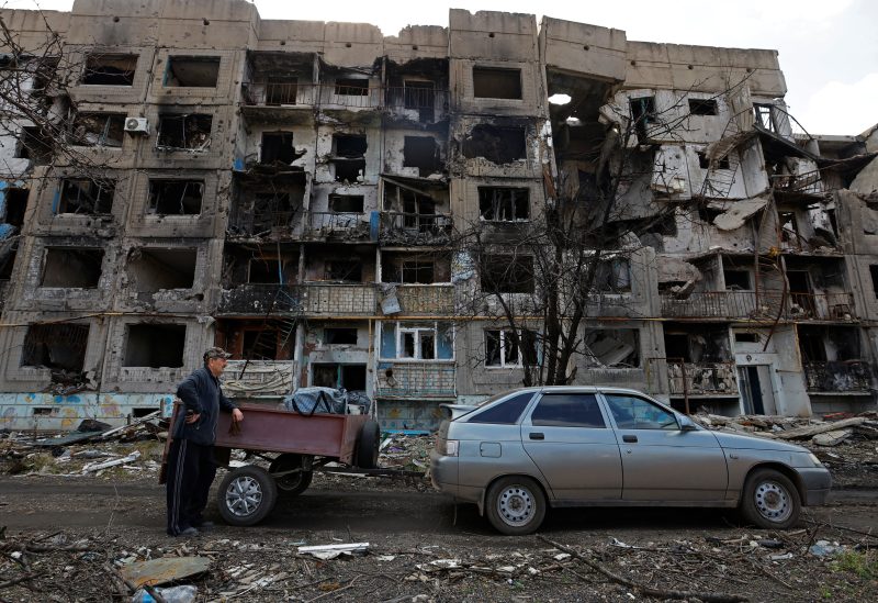 A local resident stands next to a car in front of a residential building heavily damaged in the course of Russia-Ukraine conflict, in the settlement of Toshkivka, in the Luhansk region, Russian-controlled Ukraine, March 24, 2023. REUTERS/Alexander Ermochenko