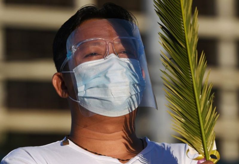 A man wearing a face mask and a face shield as protection against the coronavirus disease (COVID-19) holds palm fronds during a Palm Sunday mass outside the National Shrine of Our Mother of Perpetual Help, in Paranaque, Metro Manila, Philippines, March 28, 2021. REUTERS/Lisa Marie David