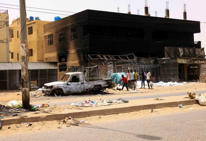 People walk near damaged car and buildings at the central market during clashes between the paramilitary Rapid Support Forces and the army in Khartoum North, Sudan April 27, 2023. REUTERS/ Mohamed Nureldin Abdallah