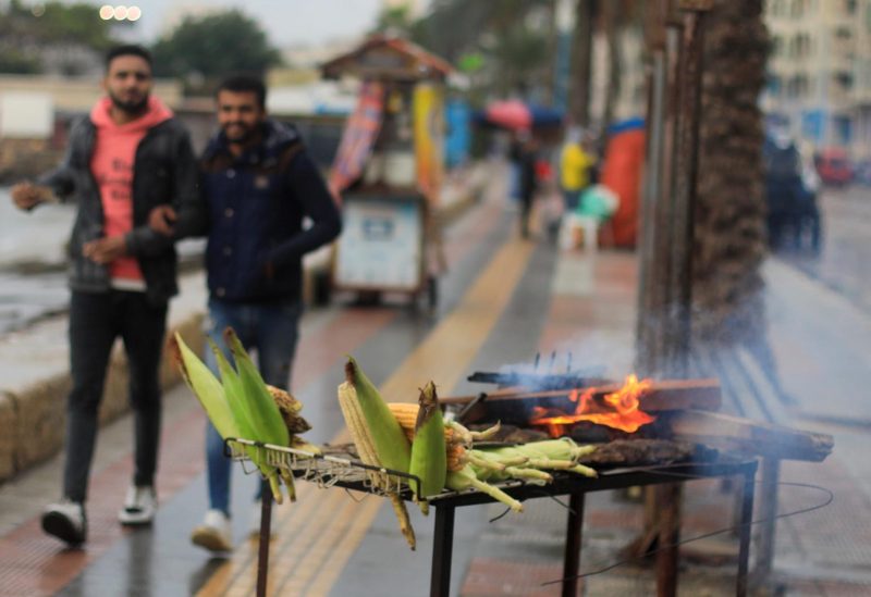 People walk next to a corn seller during rainy weather in the Mediterranean port city of Alexandria, Egypt December 31, 2021. REUTERS/Amr Abdallah Dalsh