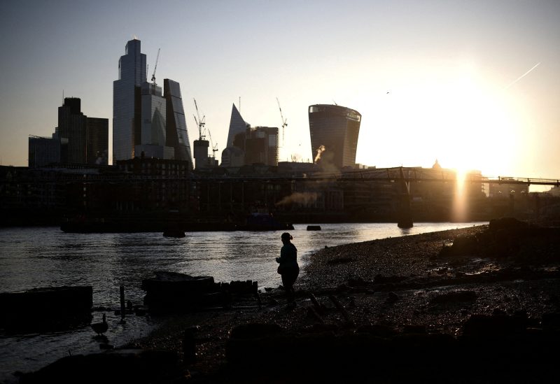 A person stands on the bank of the River Thames during sunrise, with the City of London financial district in the background, in London, Britain, April 4, 2023. REUTERS/Henry Nicholls